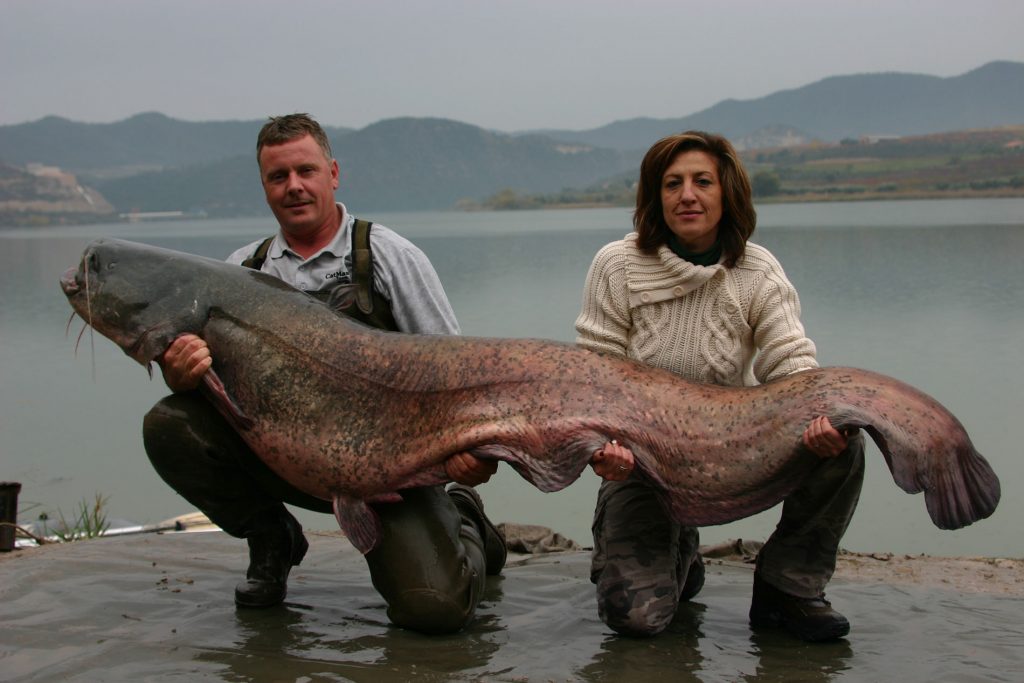 Colin Bunn holding a huge catfish on a cloudy day with the river in the background